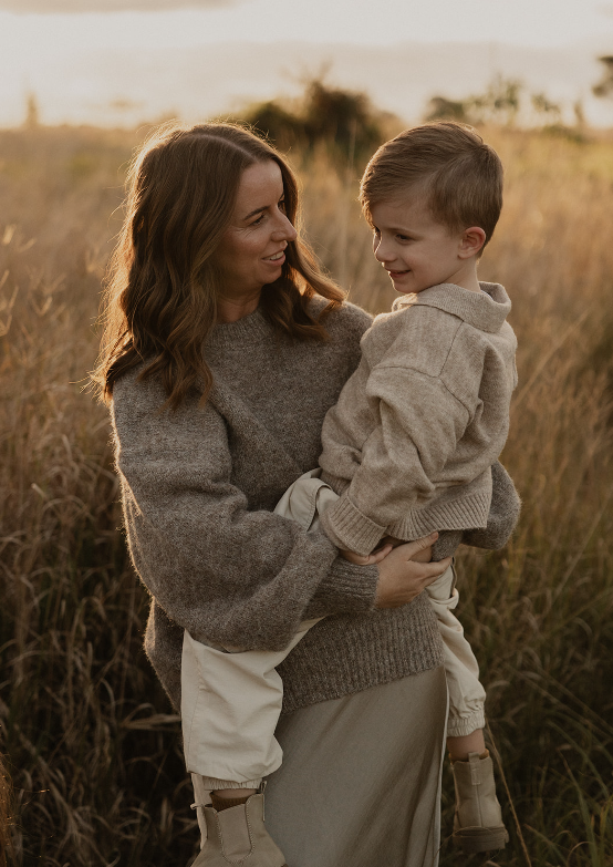 A mother holding her young son, the two of them talking closely in a golden field